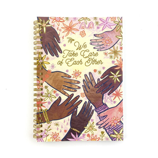 Spiral Bound notebook with hand drawn artwork of multi racial hands and flowers. In the center text says We Take Care of Each Other.
